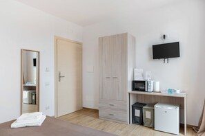 Ein Zimmer mit einem Bett, einem Kleiderschrank, einem Schreibtisch mit Mikrowelle, einem kleinen Kühlschrank und einem an der Wand befestigten Fernseher.