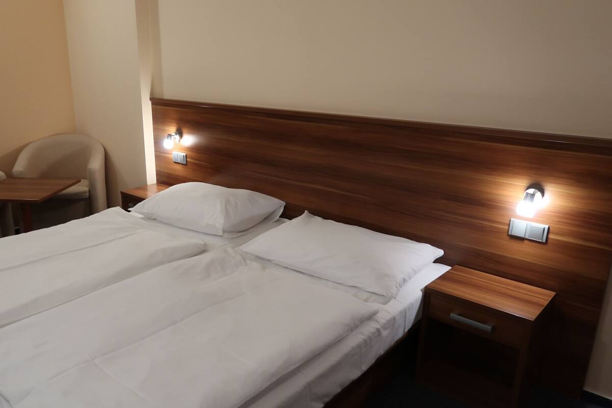 A double bed with white linens, two bedside tables, a wooden headboard, and two wall-mounted light fixtures.