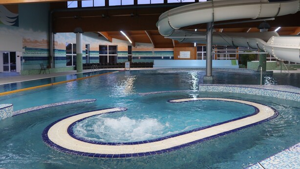 A large indoor swimming pool with a wave feature, surrounded by a tiled deck and wooden beams. - Private Luxury Apartments (Frymburk)