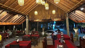 An outdoor restaurant with wooden tables and chairs, hanging lanterns, and a view of the street at night. - Ginis Beach Resort (Kamala)