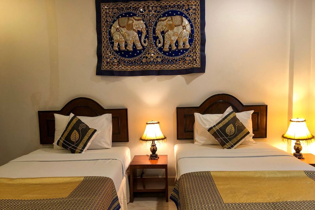 Two double beds with headboards, bedside tables with lamps, and a wall hanging above.