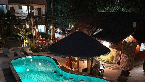 A swimming pool with a tiled edge, surrounded by lounge chairs and a bar area with a thatched roof. - Ginis Beach Resort (Kamala)