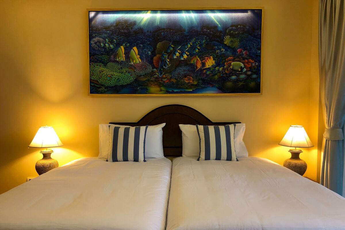 A double bed with two pillows, two bedside lamps, and a large painting of an underwater scene above the bed.