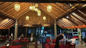 An outdoor dining area with wooden tables and chairs, hanging lanterns, and a thatched roof structure. - Ginis Beach Resort (Kamala)