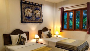 A hotel room with two beds, a decorative wall hanging, a window with curtains, and a view of greenery outside. - Ginis Beach Resort (Kamala)