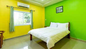 A room with a bed, a window with curtains, an air conditioner, and a green wall. - Tonrak Apartment (Hat Yai)