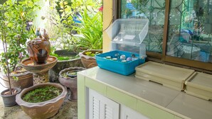 A room with a window overlooking a garden, a blue plastic container on the counter, and several potted plants. - Tonrak Apartment (Hat Yai)