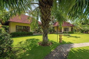 Um jardim bem cuidado com uma palmeira, um caminho de pedra e um prédio com telhado vermelho.