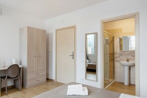 Een slaapkamer met een bed, een bureau, een kledingkast, een badkamer met een spiegel en een wastafel.