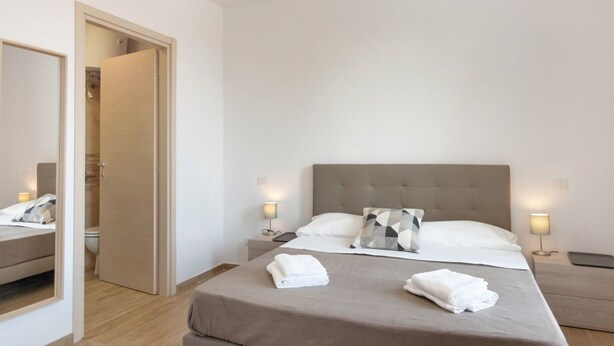 Habitación de hotel con cama, mesitas de noche, un espejo y una puerta que da a un baño.