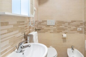 A bathroom with a sink, toilet, bidet, and a mirror.