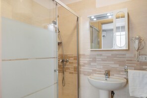 Een moderne badkamer met een douche in een glazen cabine, een wit wastafelmeubel en een spiegel erboven.