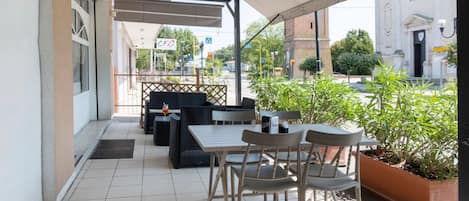 An outdoor patio with tables and chairs, a covered area, and a view of a building with a sign.