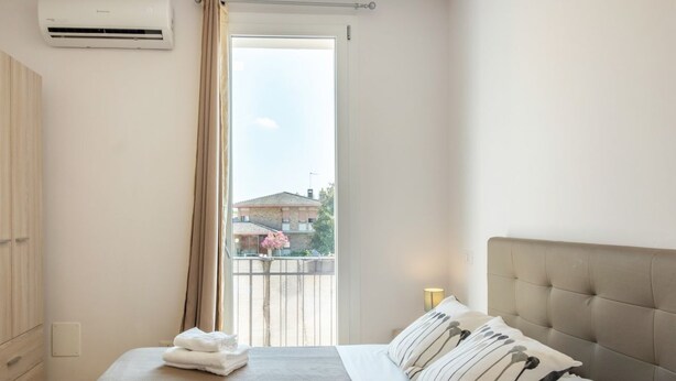 Ein Schlafzimmer mit einem Bett, einem Kleiderschrank, einem Fenster mit Vorhängen und einer Klimaanlage.