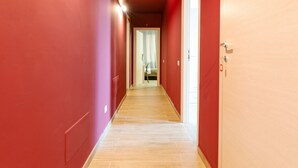 Ein Flur mit roten Wänden und Holzboden, der zu einem Zimmer mit Bett und Fenster führt.