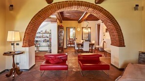 A spacious living area with a brick archway, red leather sofas, a dining table, and a kitchen in the background. - Podere Pozzangone - Your Tuscany Home (Lucignano)