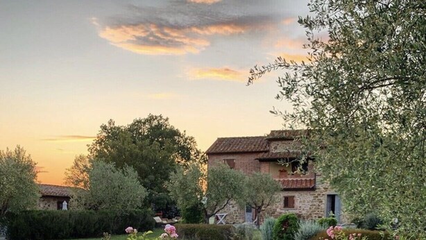 A swimming pool surrounded by lush greenery and pink flowers, with stone buildings in the background. - Podere Pozzangone - Your Tuscany Home (Lucignano)
