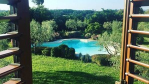 A view through a wooden gate of a swimming pool surrounded by lush greenery and trees. - Podere Pozzangone - Your Tuscany Home (Lucignano)