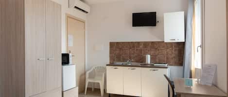 Uma cozinha compacta com micro-ondas, pia, uma cadeira branca e uma mesa pequena com uma placa.