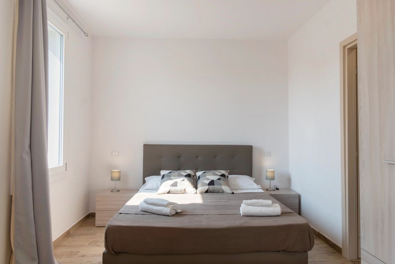 Een hotelkamer met een groot bed, twee nachtkastjes met lampen, een raam met gordijnen en een houten garderobe.