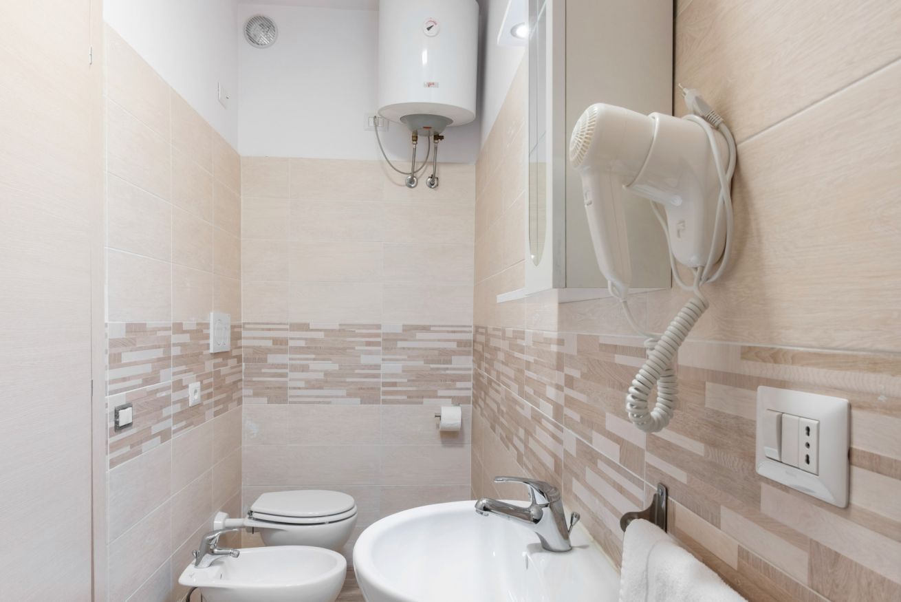Ein Badezimmer mit Toilette, Waschbecken und einem an der Wand befestigten Föhn.