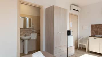 Ein Schlafzimmer mit Bett, Kleiderschrank, Schreibtisch, Stuhl, Waschbecken und Klimaanlage.
