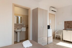 Ein Schlafzimmer mit Bett, Kleiderschrank, Schreibtisch, Stuhl, Waschbecken und Klimaanlage.