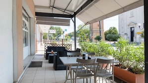 Une terrasse extérieure avec des tables et des chaises, un espace abrité et une vue sur un bâtiment portant une enseigne.