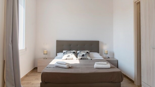 Une chambre d’hôtel avec un grand lit, deux tables de chevet avec des lampes, une fenêtre avec des rideaux et une armoire en bois.