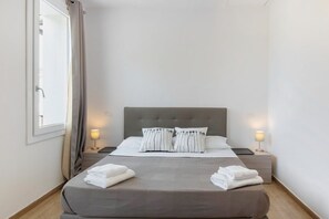 Habitación de hotel con cama, dos mesitas de noche, ventana con cortinas y vista al exterior.