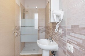 Un baño moderno con cabina de ducha de vidrio, un lavamanos blanco y un secador de pelo fijado a la pared.