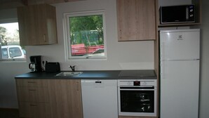 A compact kitchen with wooden cabinets, a window, a microwave, a dishwasher, and a refrigerator. - Eyvindartunga Farm Cottage (Bláskógabyggd)