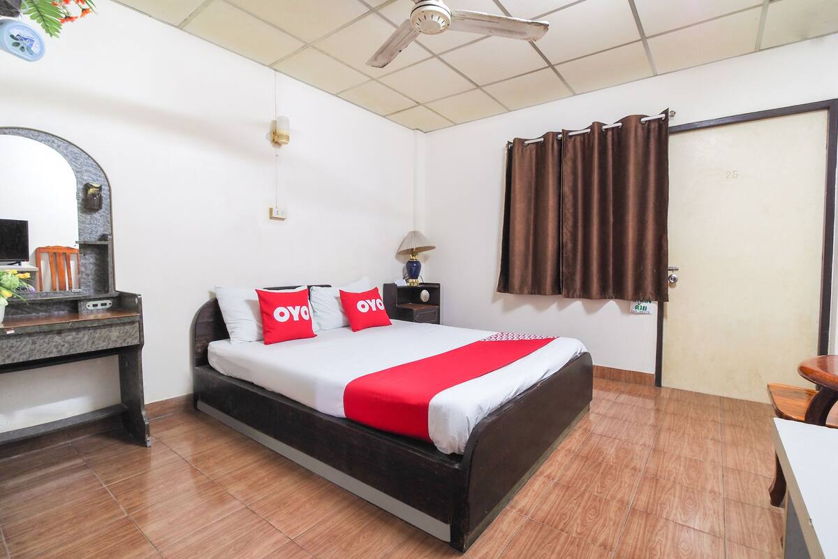 A bedroom with a bed, a desk, a mirror, a ceiling fan, and a window with curtains.