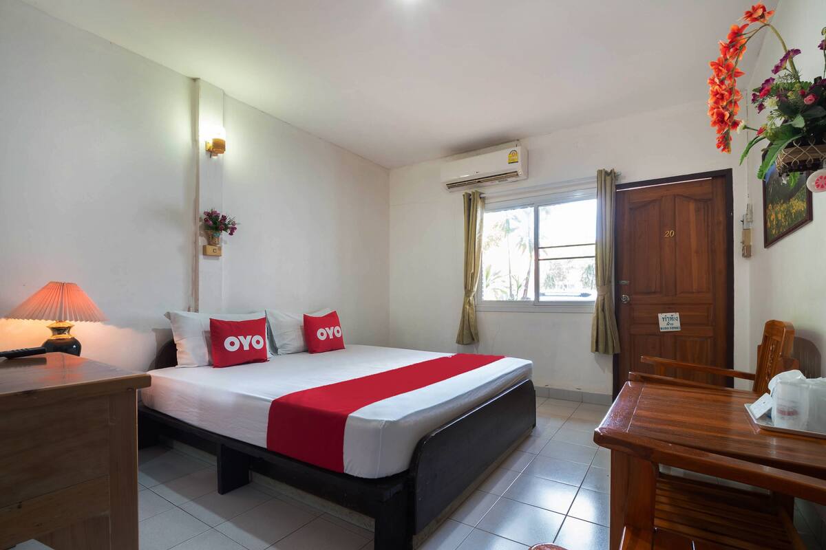 A hotel room with a bed, a desk, a chair, a window with curtains, and an air conditioning unit.