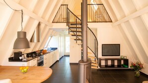 Un loft moderno con cocina, comedor y sala de estar, que presenta una estufa de leña central, una escalera y un televisor.