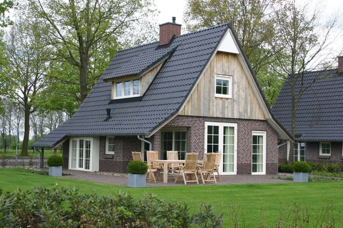 A two-story house with a steeply pitched roof, brick exterior, and a patio with outdoor furniture.