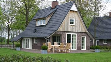 Een tweelaags huis met een steile dakschild, bakstenen gevel en een terras met buitenmeubilair.