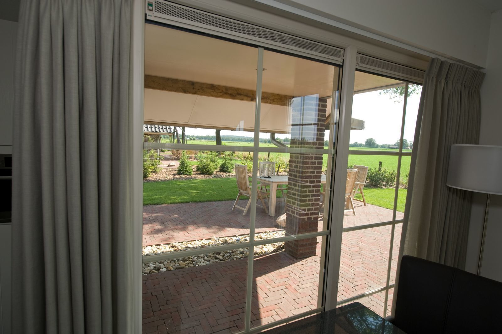 Una habitación con puerta de vidrio corredera que da a un patio exterior con suelo de ladrillo, chimenea de ladrillo y mobiliario para exteriores.