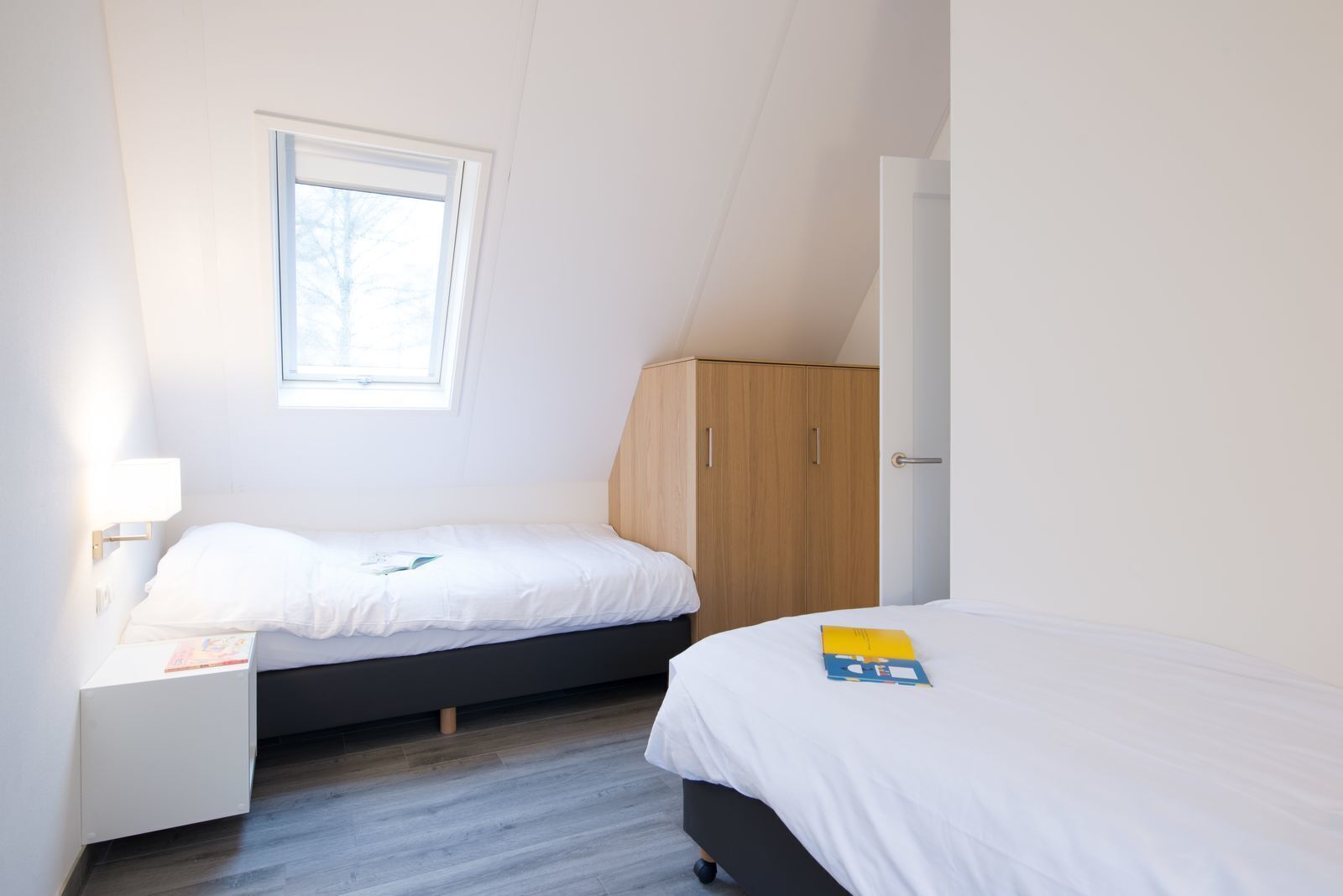 Une chambre avec deux lits, une fenêtre, une armoire et une table de chevet.