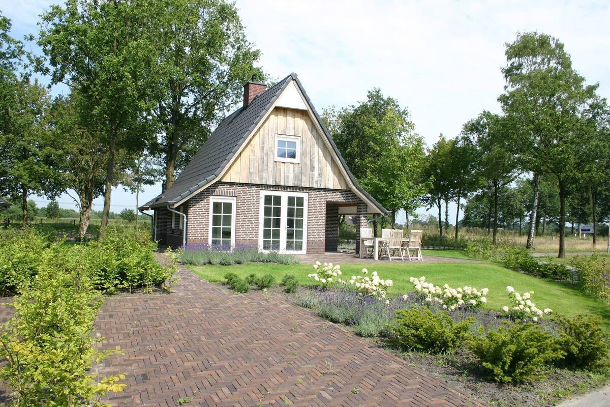 A rustic wooden house with a brick facade, large windows, and a garden with flowers and shrubs.