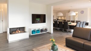 Una sala de estar moderna con chimenea, un televisor de pantalla plana, una zona de comedor con mesa y sillas, y un sofá.
