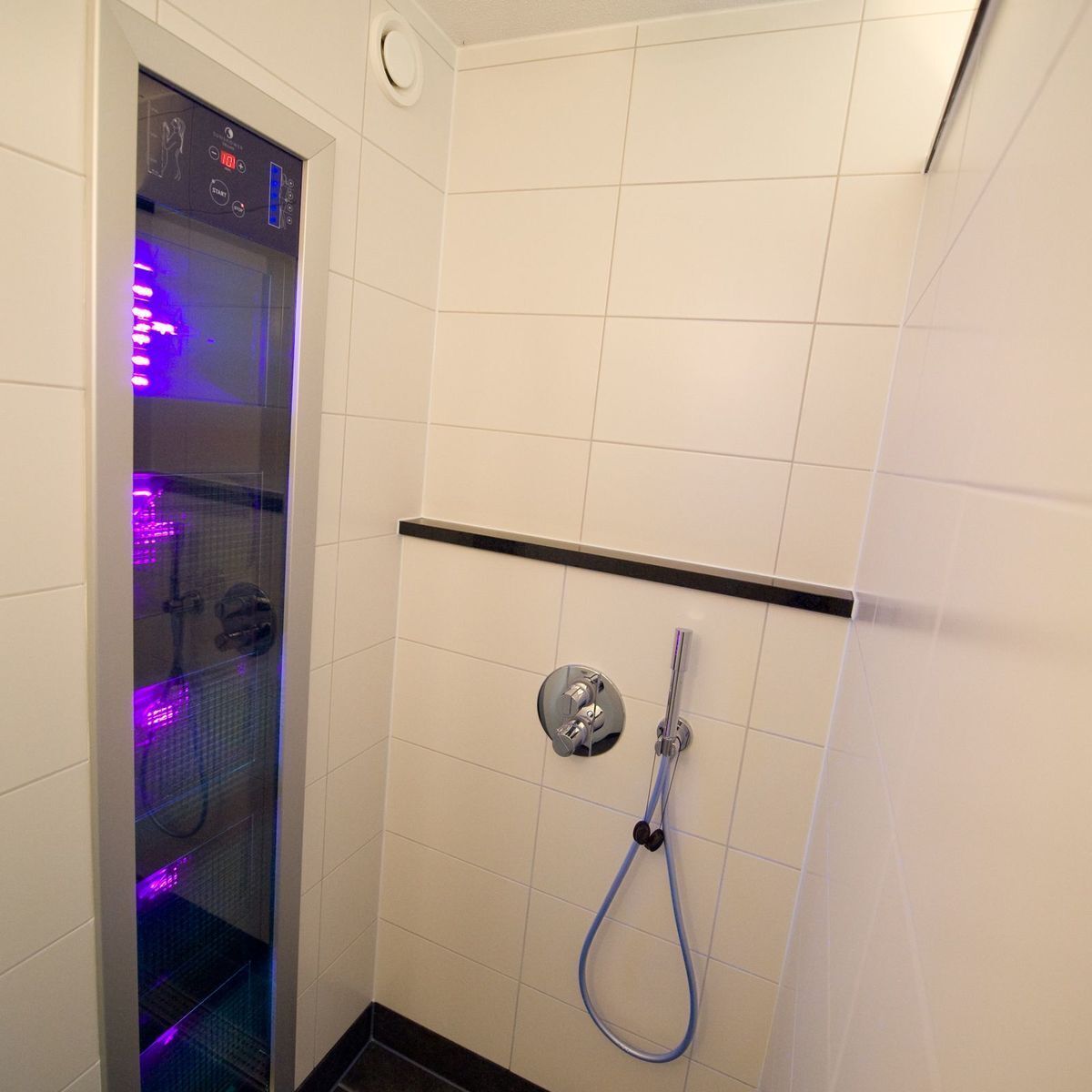 A modern shower with a control panel, a handheld showerhead, and a glass enclosure with purple lighting.