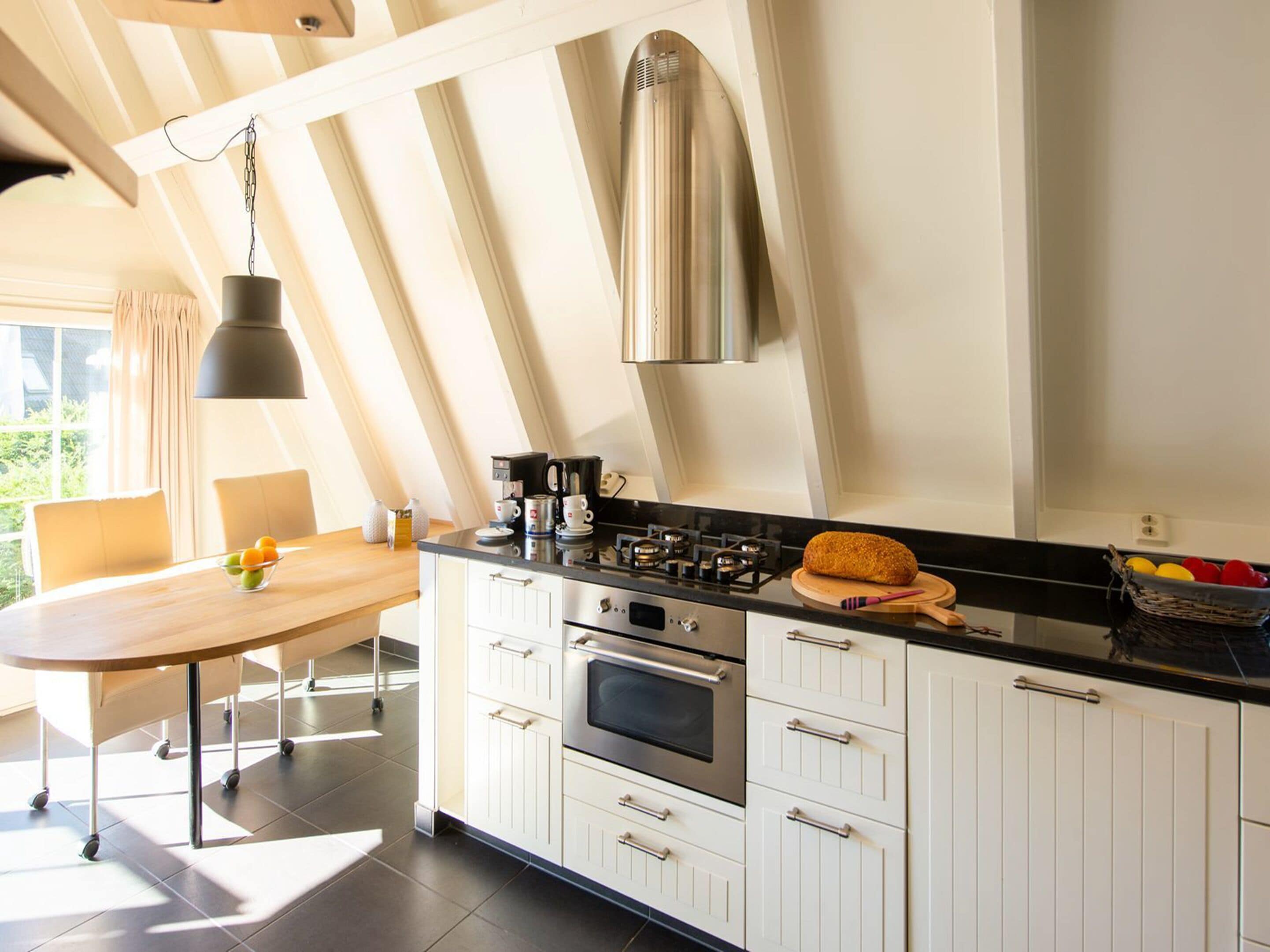 Una cocina moderna con armarios blancos, encimera negra y campana extractora de acero inoxidable.