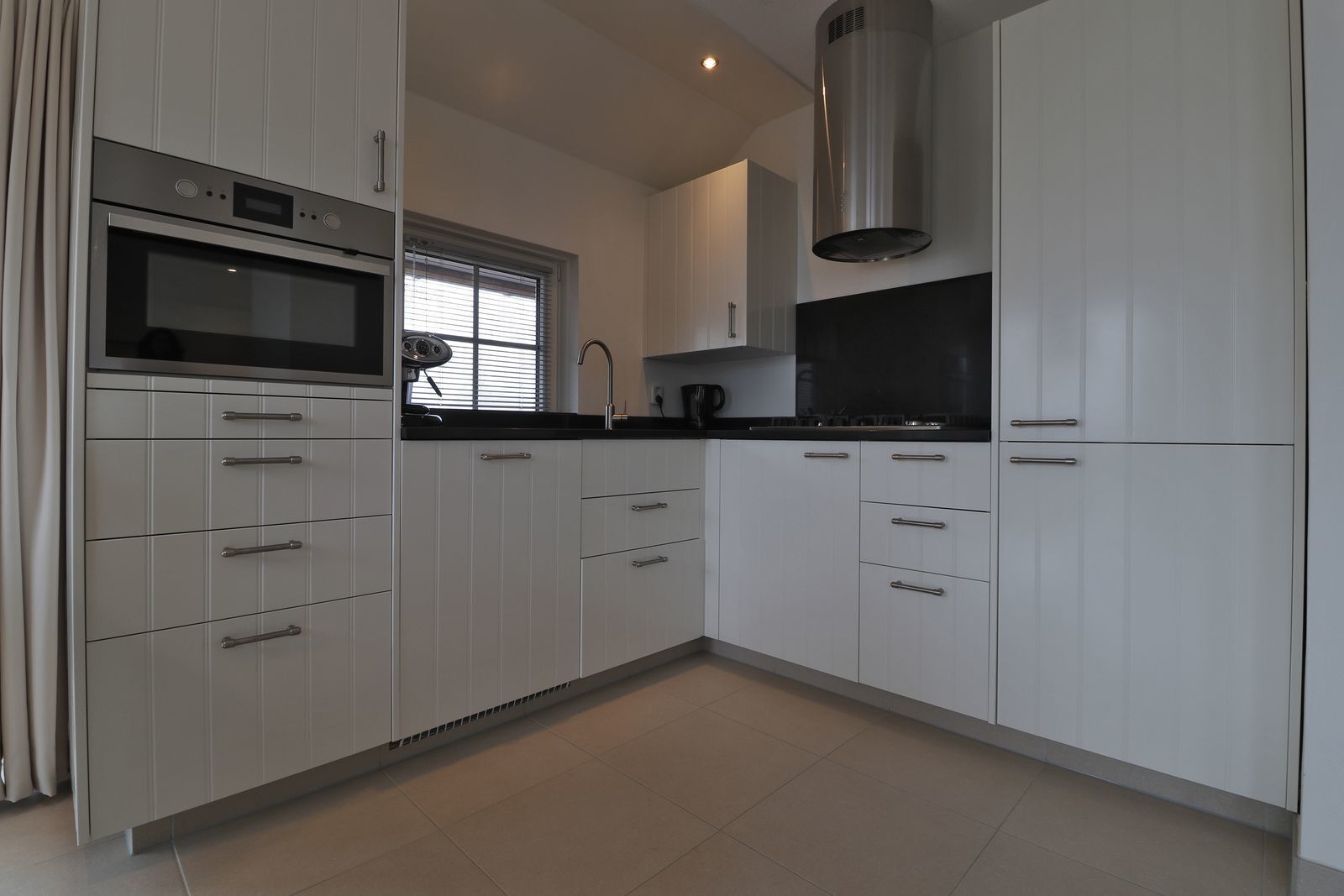 A modern kitchen with white cabinets, a built-in oven, a stainless steel range hood, and a black countertop.