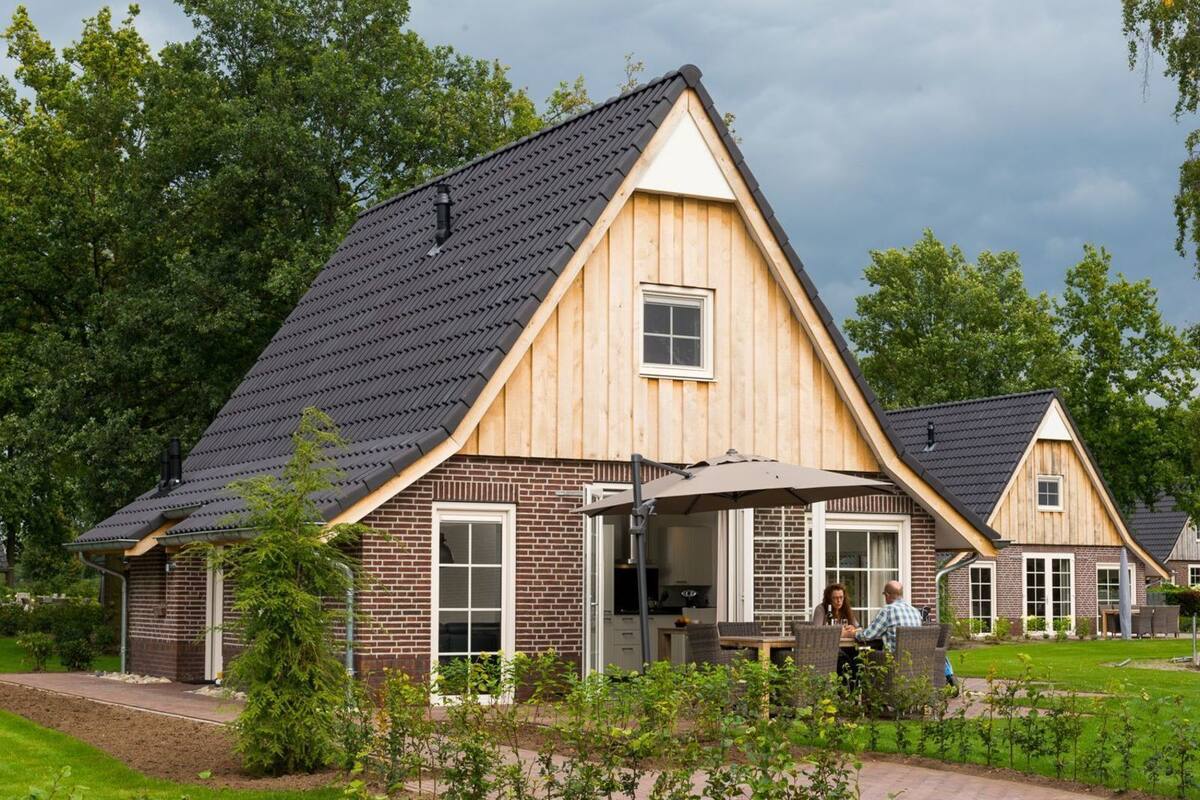 A wooden house with a sloped roof and brick exterior, featuring a patio area with outdoor furniture.