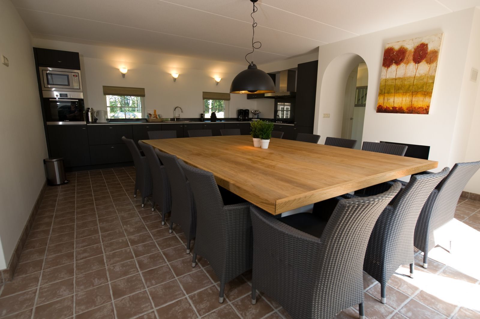Una cocina moderna con un amplio comedor de madera, sillas de mimbre oscuro y una lámpara colgante.
