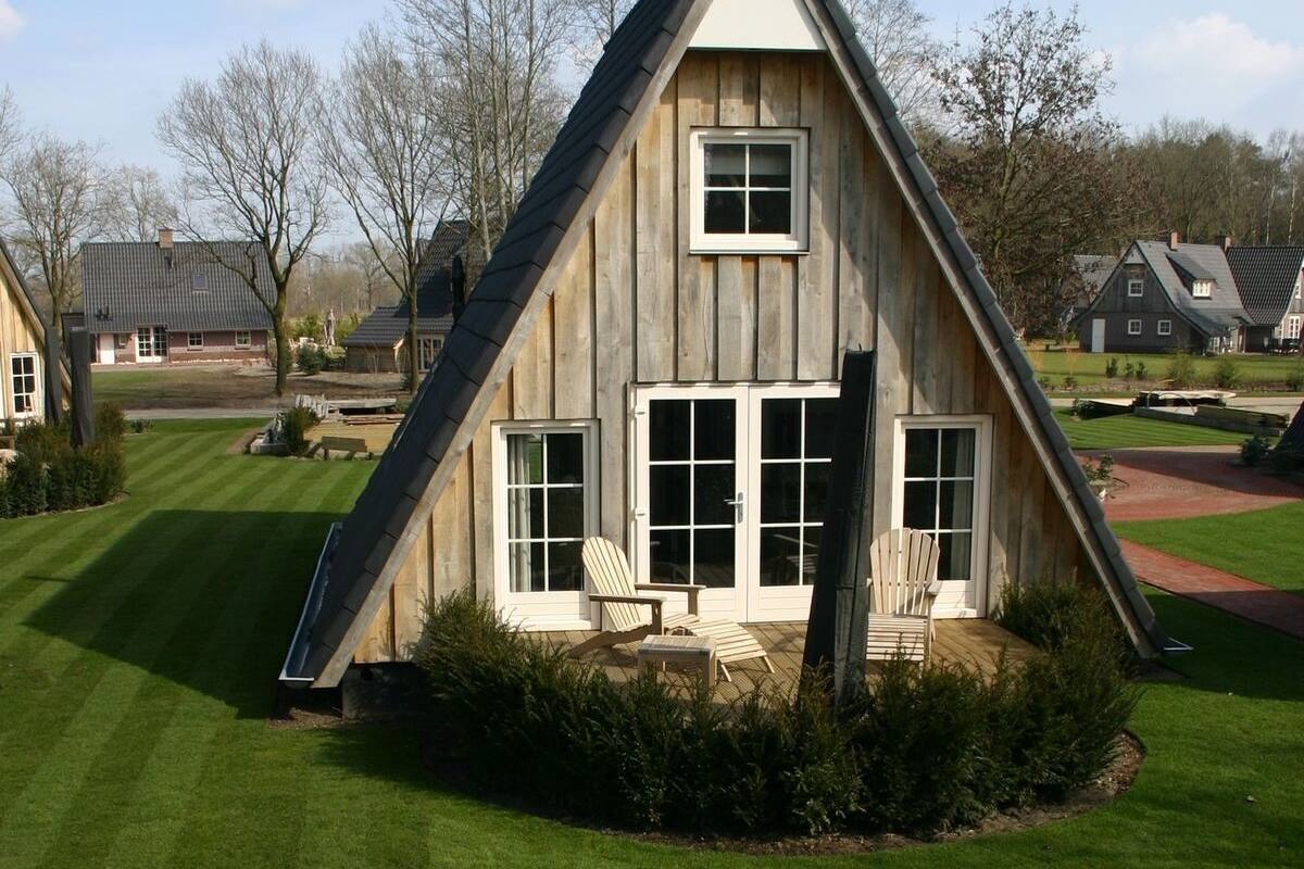A wooden house with a steep gable roof, large windows, and a small porch with chairs.