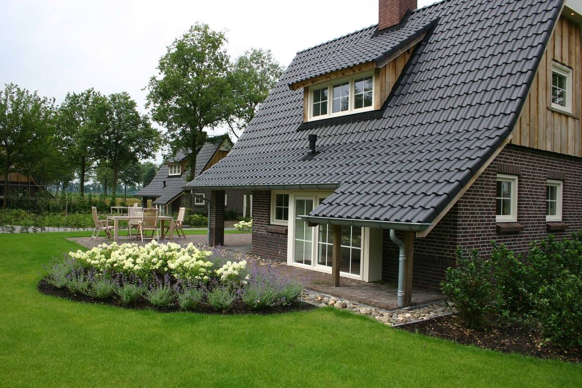 A house with a sloped roof, a brick exterior, and a garden with flowers and shrubs.