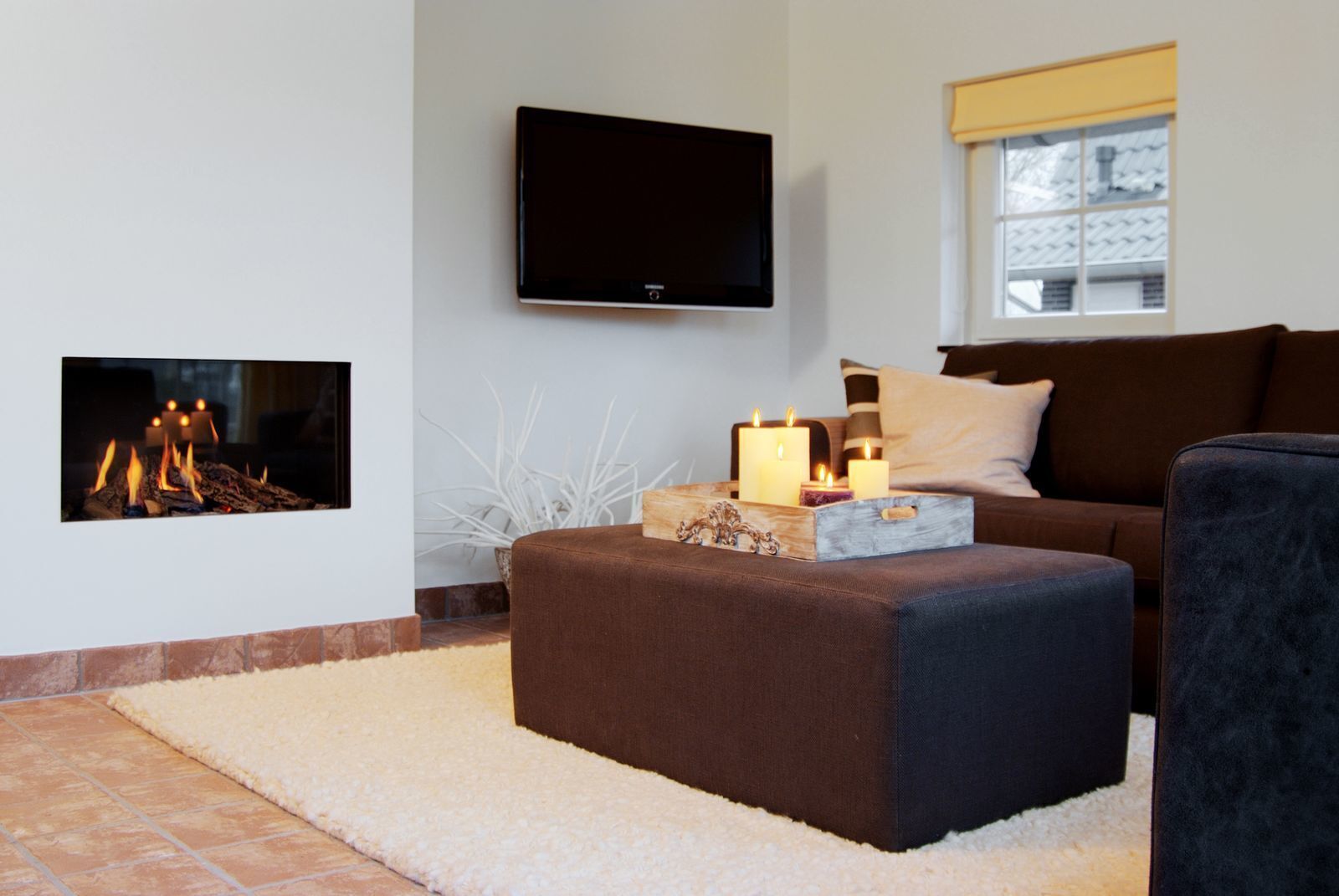 A living room with a fireplace, a television mounted on the wall, and a sofa with cushions.