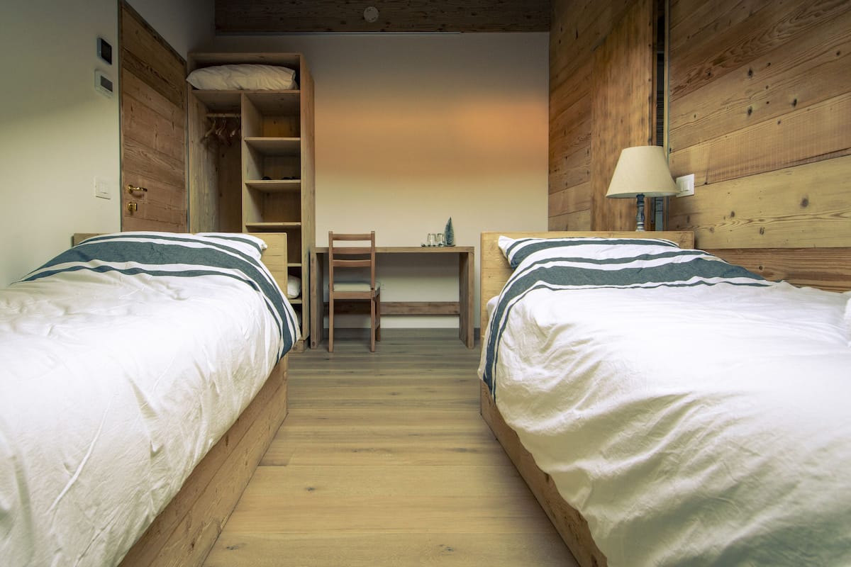 Quarto com duas camas, uma escrivaninha e uma cadeira.